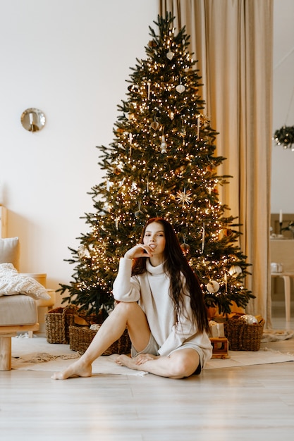 bella donna in un maglione invernale bianco sullo sfondo di un albero di Natale