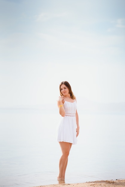 Bella donna in un vestito bianco che cammina sulla spiaggia.