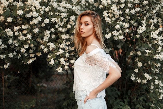 Bella donna in una maglietta di pizzo bianco con pantaloncini di jeans vicino a un cespuglio con fiori