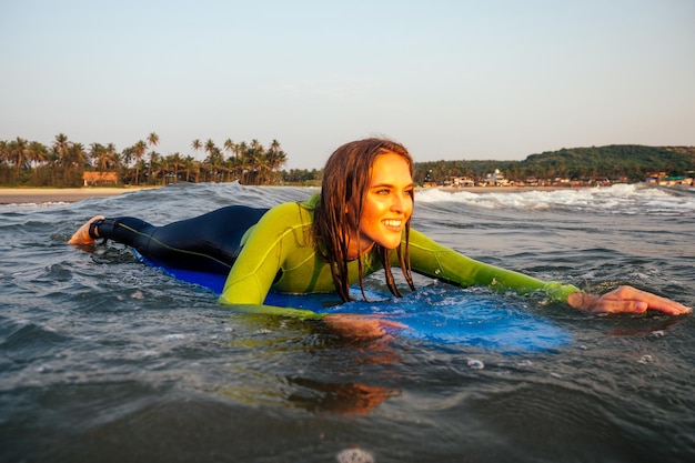 Bella donna in una muta da sub per nuotare facendo surf nell'Oceano Indiano sullo sfondo cielo al tramonto e onde ragazza surfista professionista in una muta che fa sport in mare estremo, adrenalina e giovinezza