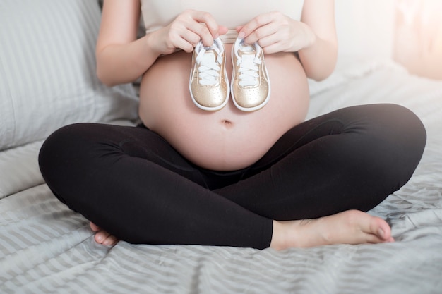 Bella donna incinta asiatica in attesa del suo bambino con piccole scarpe