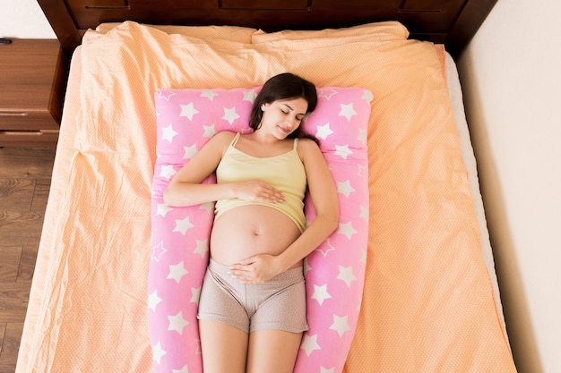 Bella donna incinta che dorme con il cuscino del corpo sul letto