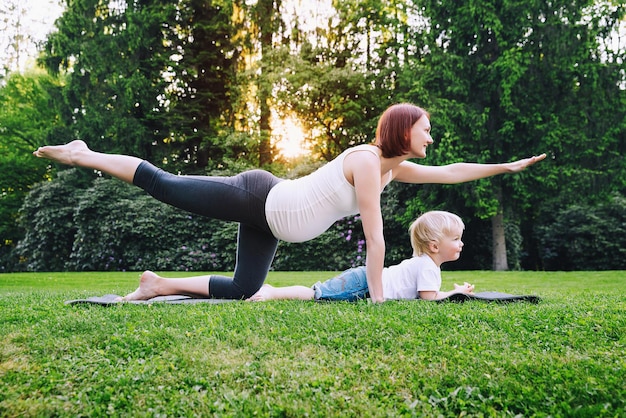 Bella donna incinta che fa yoga con il piccolo figlio sulla natura all'aperto