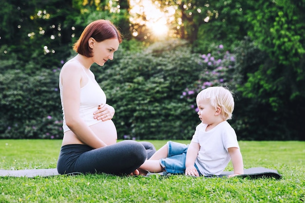 Bella donna incinta che fa yoga con il piccolo figlio sulla natura all'aperto