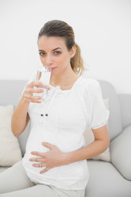 Bella donna incinta che tocca la sua pancia bevendo un bicchiere d&#39;acqua