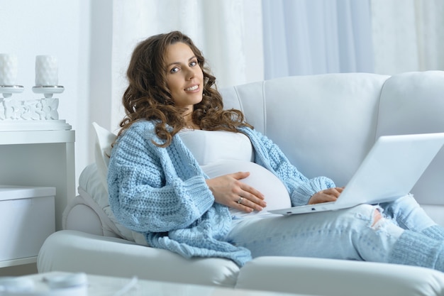 Bella donna incinta con lunghi capelli scuri e laptop