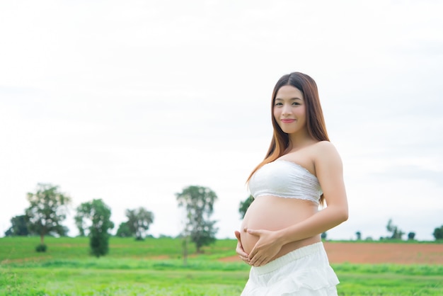 Bella donna incinta del primo piano nei campi sul cielo bianco, nuvola molle sul cielo