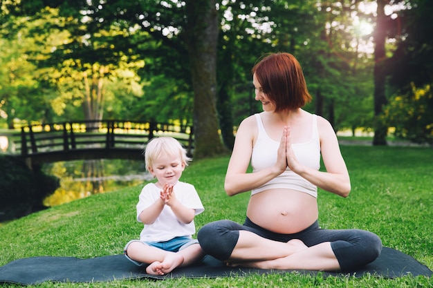 Bella donna incinta e madre con il suo bambino bambino carino nella posizione del loto che fa yoga