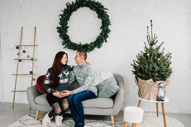 Bella donna incinta e uomo in maglioni morbidi vicino all'albero Anno nuovo e Buon Natale