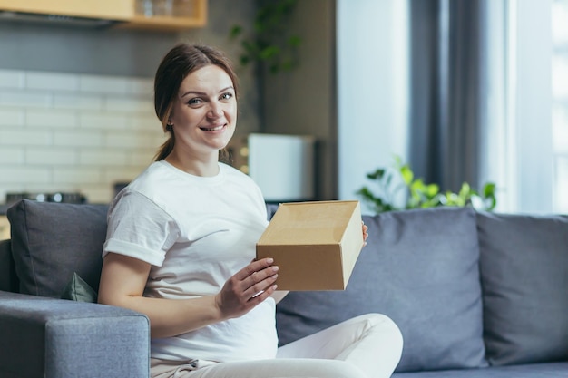 Bella donna incinta ha ricevuto un pacco dal corriere regalo pacchetto casa Si siede sul divano a casa apre una scatola di carta gioisce sorrisi