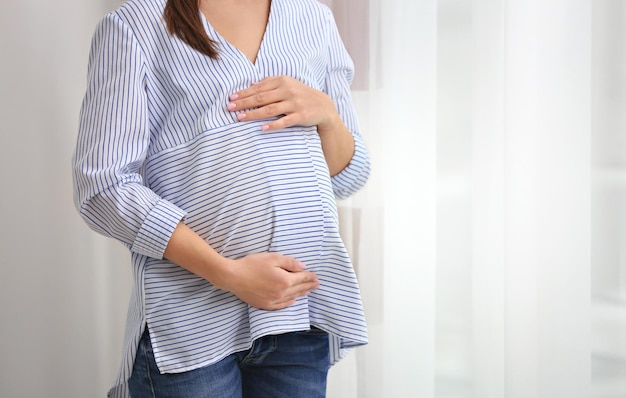 Bella donna incinta in piedi vicino alla finestra a casa