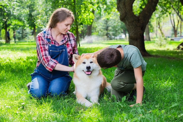 Bella donna incinta in tuta di jeans blu con suo figlio e il cane giapponese Akita inu nel parco