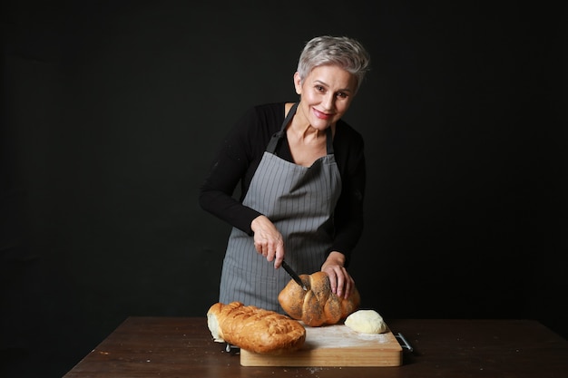 bella donna invecchiata in un grembiule, taglia il pane