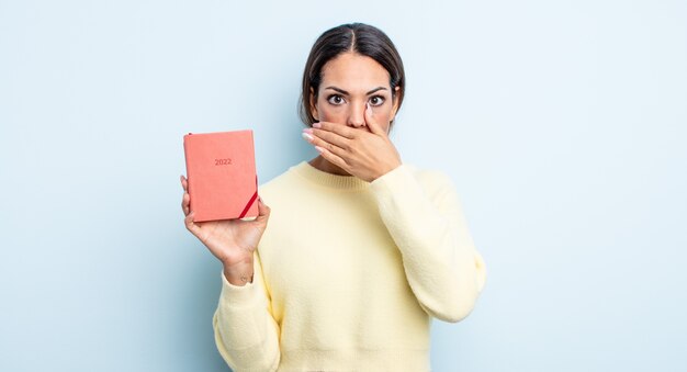 Bella donna ispanica che copre la bocca con le mani con uno scioccato. concetto di agenda