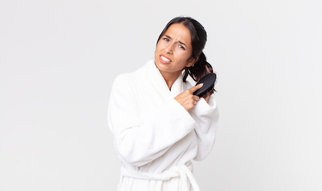 Bella donna ispanica che indossa accappatoio e tiene in mano una spazzola per capelli