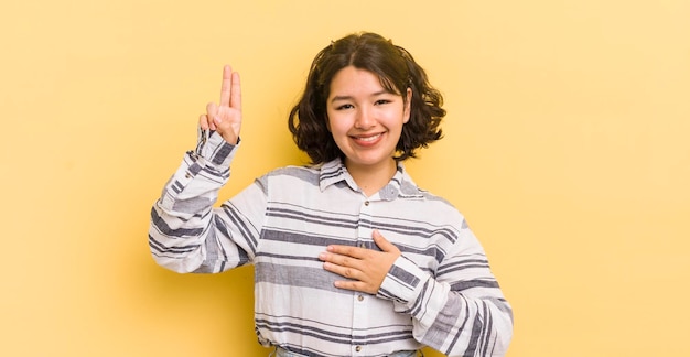 Bella donna ispanica che sembra felice, sicura di sé e degna di fiducia, sorridente e mostra il segno della vittoria con un atteggiamento positivo