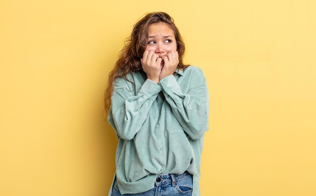 Bella donna ispanica che sembra preoccupata, ansiosa, stressata e spaventata, che si morde le unghie e guarda allo spazio laterale della copia