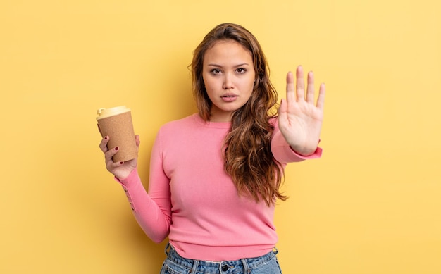 Bella donna ispanica che sembra seria mostrando il palmo aperto facendo il gesto di arresto porta via il concetto di caffè