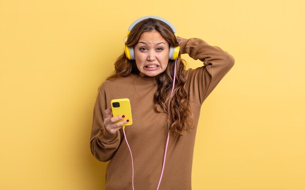 Bella donna ispanica che si sente stressata, ansiosa o spaventata, con le mani sulla testa. cuffie e concetto di smartphone