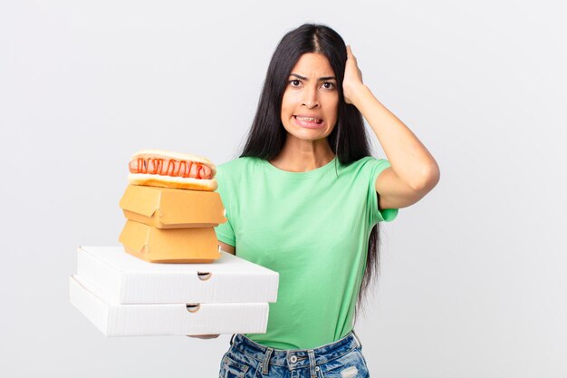 Bella donna ispanica che si sente stressata, ansiosa o spaventata, con le mani sulla testa e tiene in mano scatole di fast food da asporto