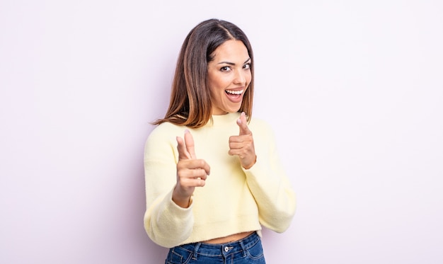 Bella donna ispanica che sorride con un atteggiamento positivo, di successo e felice che punta alla telecamera, facendo il segno della pistola con le mani