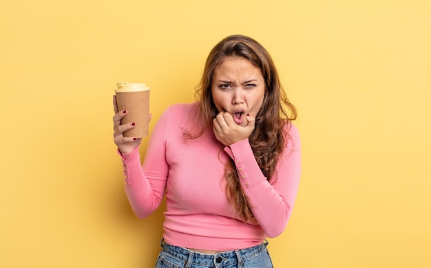 Bella donna ispanica con la bocca e gli occhi spalancati e la mano sul mento. portare via il concetto di caffè