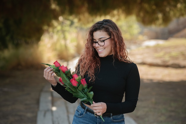 Bella donna latina con gli occhiali innamorata di alcune rose nel campo all'aperto