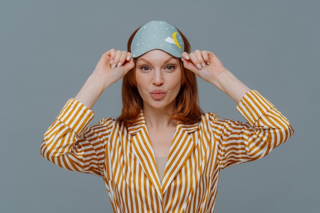 Bella donna lentigginosa allo zenzero indossa maschera da notte e pigiama a righe