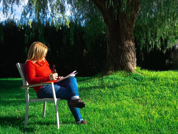 Bella donna matura che gode di un soleggiato mezzogiorno invernale all'aperto leggendo un libro in giardino