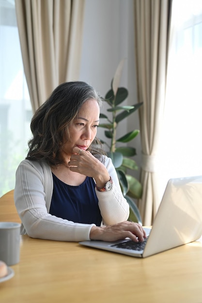 Bella donna matura che legge notizie online controllando i social media sul computer portatile Concetto di tecnologia anziana