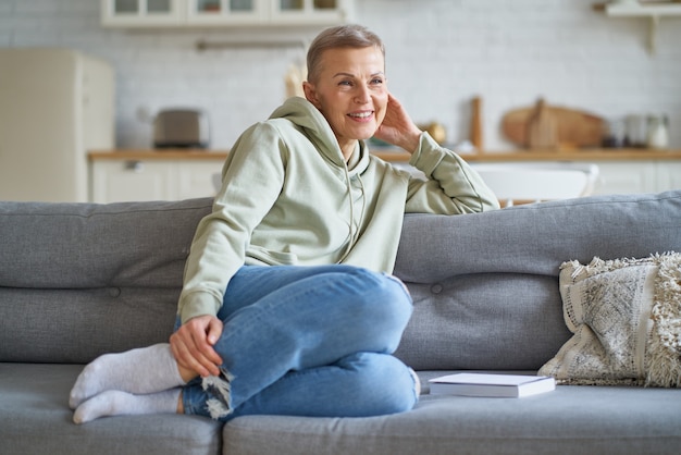 Bella donna matura in abiti casual che sogna qualcosa mentre si rilassa sul divano di casa