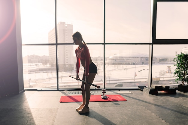 Bella donna muscolare che fa esercizio con il bastone relativo alla ginnastica in una palestra. Muro svedese in uno sfondo