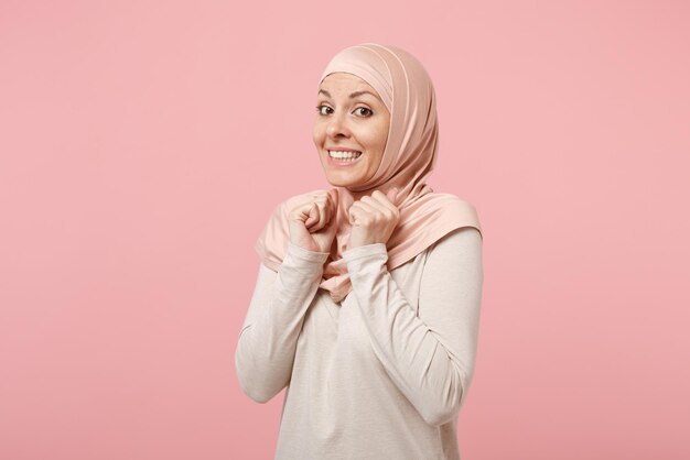 Bella donna musulmana araba in abiti leggeri hijab in posa isolata su sfondo rosa. Concetto di stile di vita religioso della gente. Mock up spazio di copia. Stringere i pugni, aspettare un momento speciale, esprimere desideri.