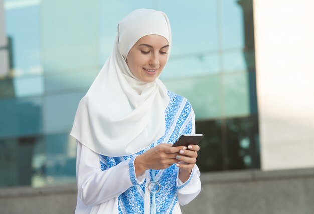 Bella donna musulmana che manda un sms su un telefono cellulare all'aperto.