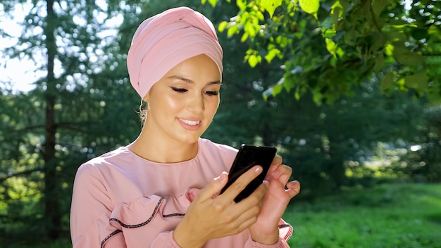 Bella donna musulmana in turbante con telefono sullo sfondo degli alberi.