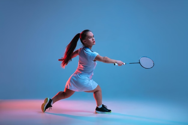 Bella donna nana che pratica a badminton isolata su sfondo blu in luce al neon