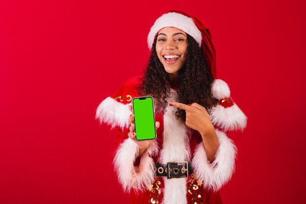 Bella donna nera brasiliana vestita da babbo natale vestiti di natale in possesso di un telefono cellulare con schermo cromatico