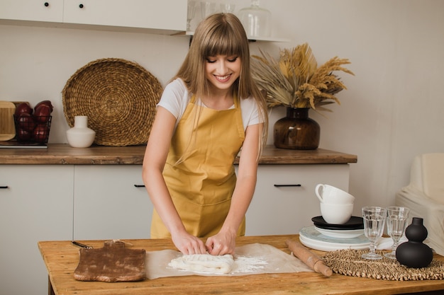 Bella donna pasticcere, panettiere o casalinga in un grembiule impasta la pasta in cucina e sorride