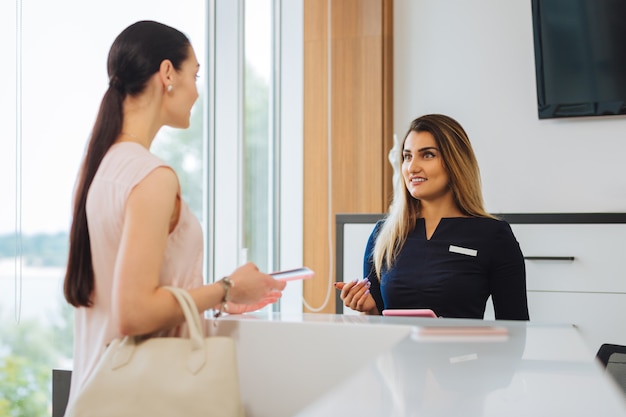 Bella donna piacevole che parla con l'addetto alla reception mentre ha un appuntamento nel salone di bellezza