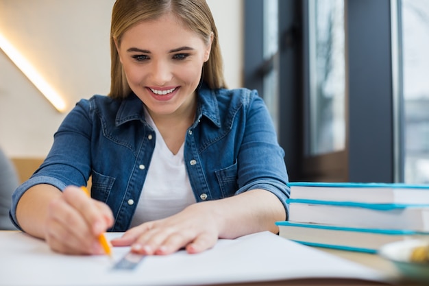 Bella donna positiva felice seduta al tavolo e facendo un disegno mentre si lavora al suo progetto