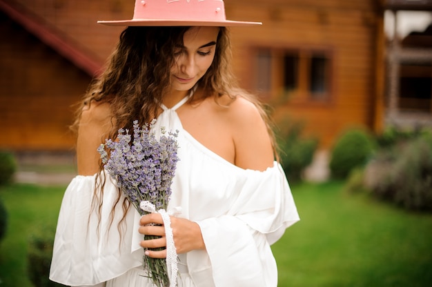 Bella donna riccia vestita in abito bianco con bouquet di lavanda