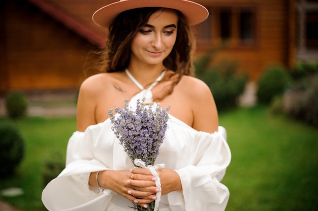 Bella donna riccia vestita in abito bianco con bouquet di lavanda