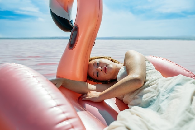 Bella donna sdraiata sul materasso galleggiante galleggiante sul mare rosa