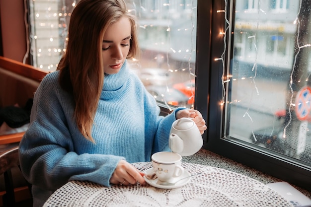Bella donna seduta al bar e beve caffè caldo vicino alla finestra