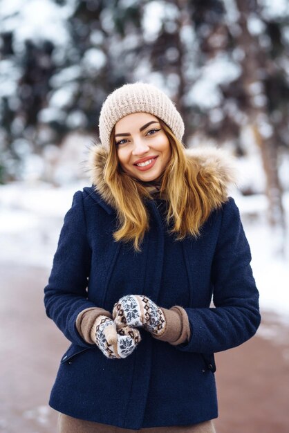 Bella donna si erge tra alberi innevati nella foresta invernale Moda donna nel parco invernale