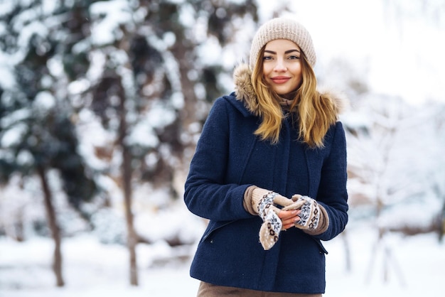 Bella donna si erge tra alberi innevati nella foresta invernale Moda donna nel parco invernale