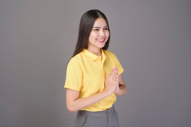 Bella donna sicura di sé sta salutando (Thai wai) per mostrare rispetto sul grigio