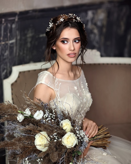 Bella donna snella in un lussuoso abito da sposa in Studio. Ritratto della sposa con un bouquet bianco tra le mani.
