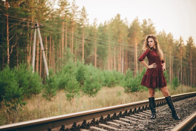 Bella donna sognante in abito cremisi godersi la natura nella foresta sulla ferrovia