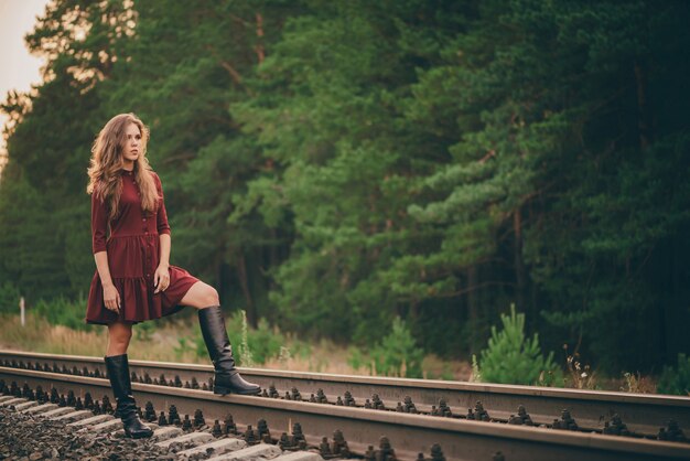 Bella donna sognante in abito cremisi godersi la natura nella foresta sulla ferrovia